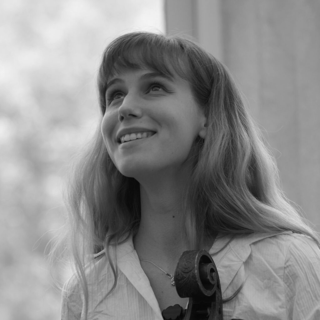 Close-up of a smiling woman looking upward, with a guitar hanging at her chest in the black-and-white photo.